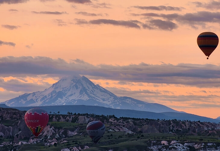 Gün doğumunda Aşk Vadisi üzerinde süzülen sıcak hava balonları ve arka planda Erciyes Dağı silueti